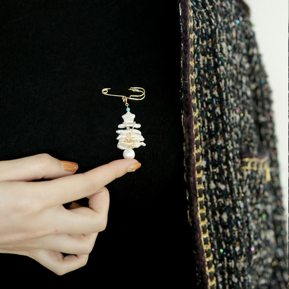 One hand holds up the baroque pearl brooch on the dress.