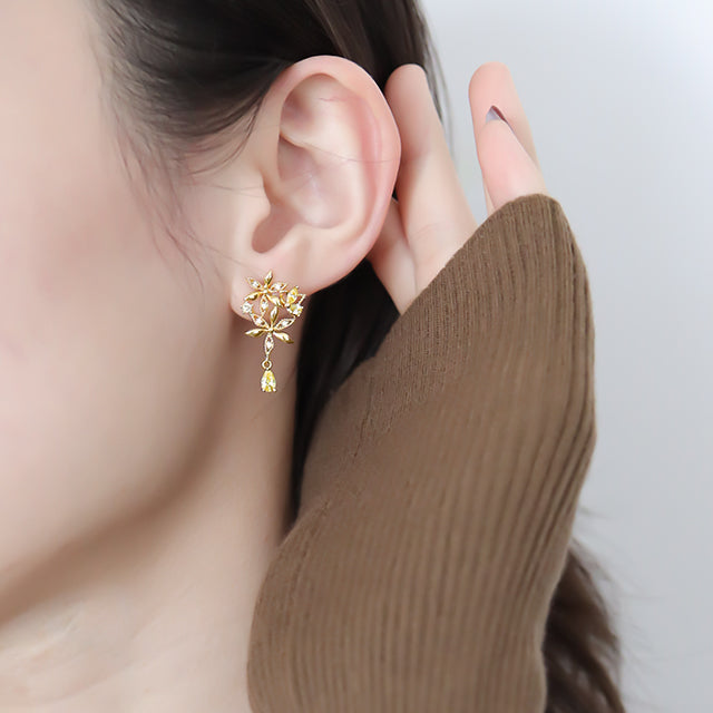 Gold hanging earrings with yellow diamond on women ear.